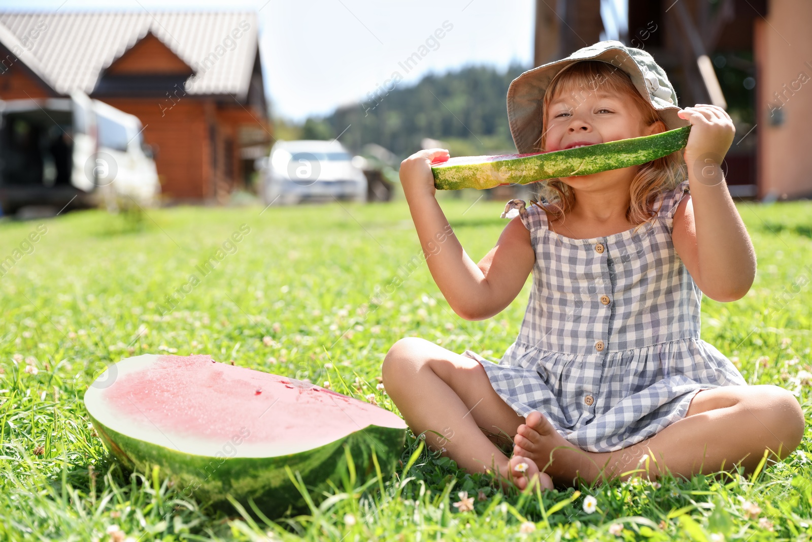 Photo of Cute little girl eating juicy watermelon on green grass outdoors