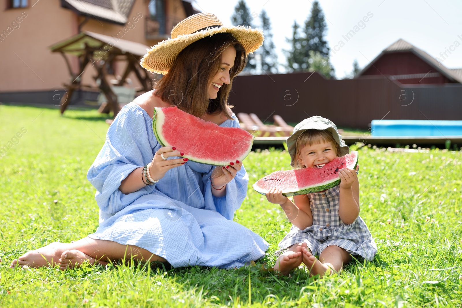 Photo of Mother and her daughter eating juicy watermelon on green grass outdoors