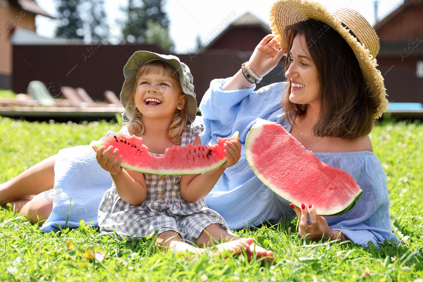 Photo of Mother and her daughter with slices of juicy watermelon on green grass outdoors