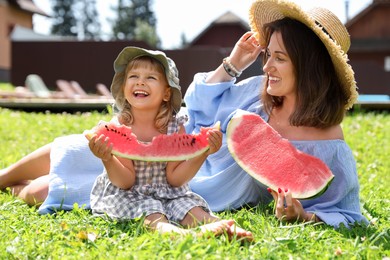 Photo of Mother and her daughter with slices of juicy watermelon on green grass outdoors