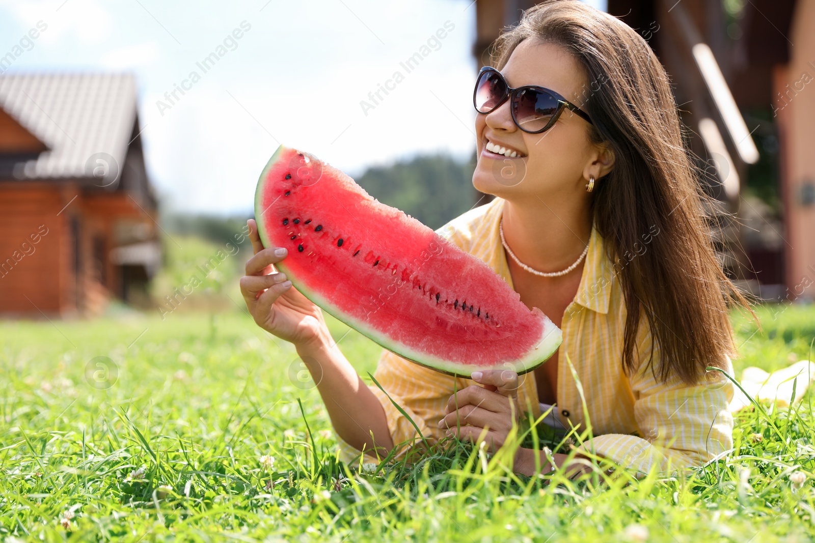 Photo of Happy woman holding slice of juicy watermelon on green grass outdoors