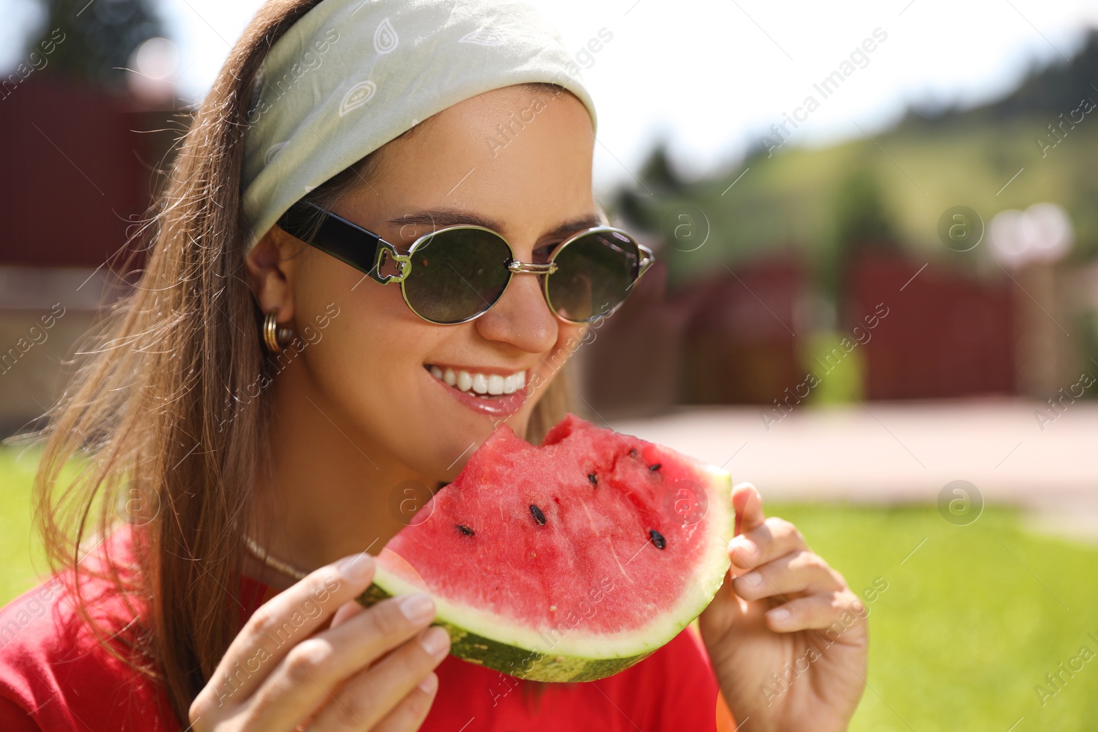 Photo of Happy woman in sunglasses eating juicy watermelon outdoors