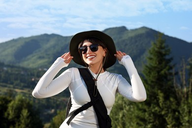 Photo of Smiling woman in sunglasses with backpack in beautiful mountains