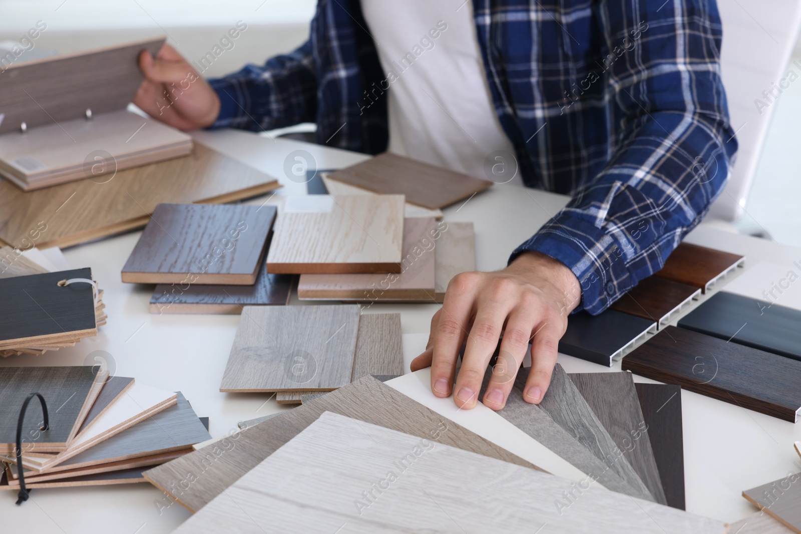 Photo of Man choosing wooden flooring among different samples at table, closeup