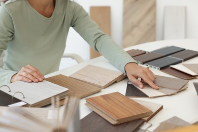 Photo of Woman choosing wooden flooring among different samples at table, closeup