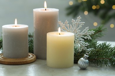 Photo of Burning candles, baubles and fir tree branches on white textured table, closeup