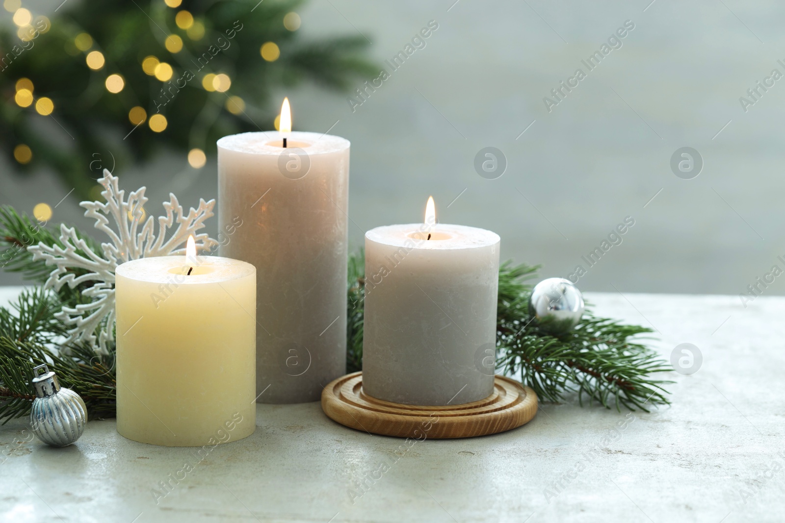 Photo of Burning candles, baubles and fir tree branches on white textured table, closeup