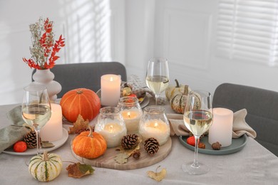 Photo of Autumn place setting with burning candles, glasses of wine and decor on table indoors