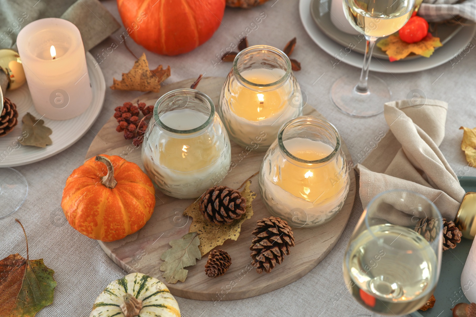 Photo of Burning candles, glasses of wine and autumn decor on table, closeup