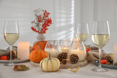 Photo of Autumn place setting with burning candles, glasses of wine and decor on table indoors