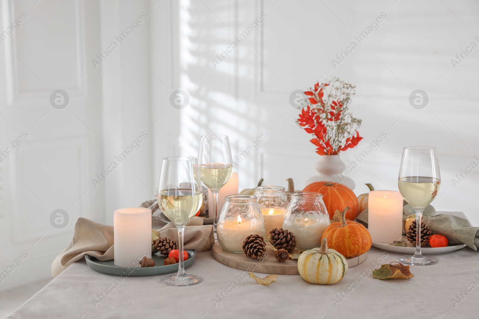 Photo of Autumn place setting with burning candles, glasses of wine and decor on table indoors