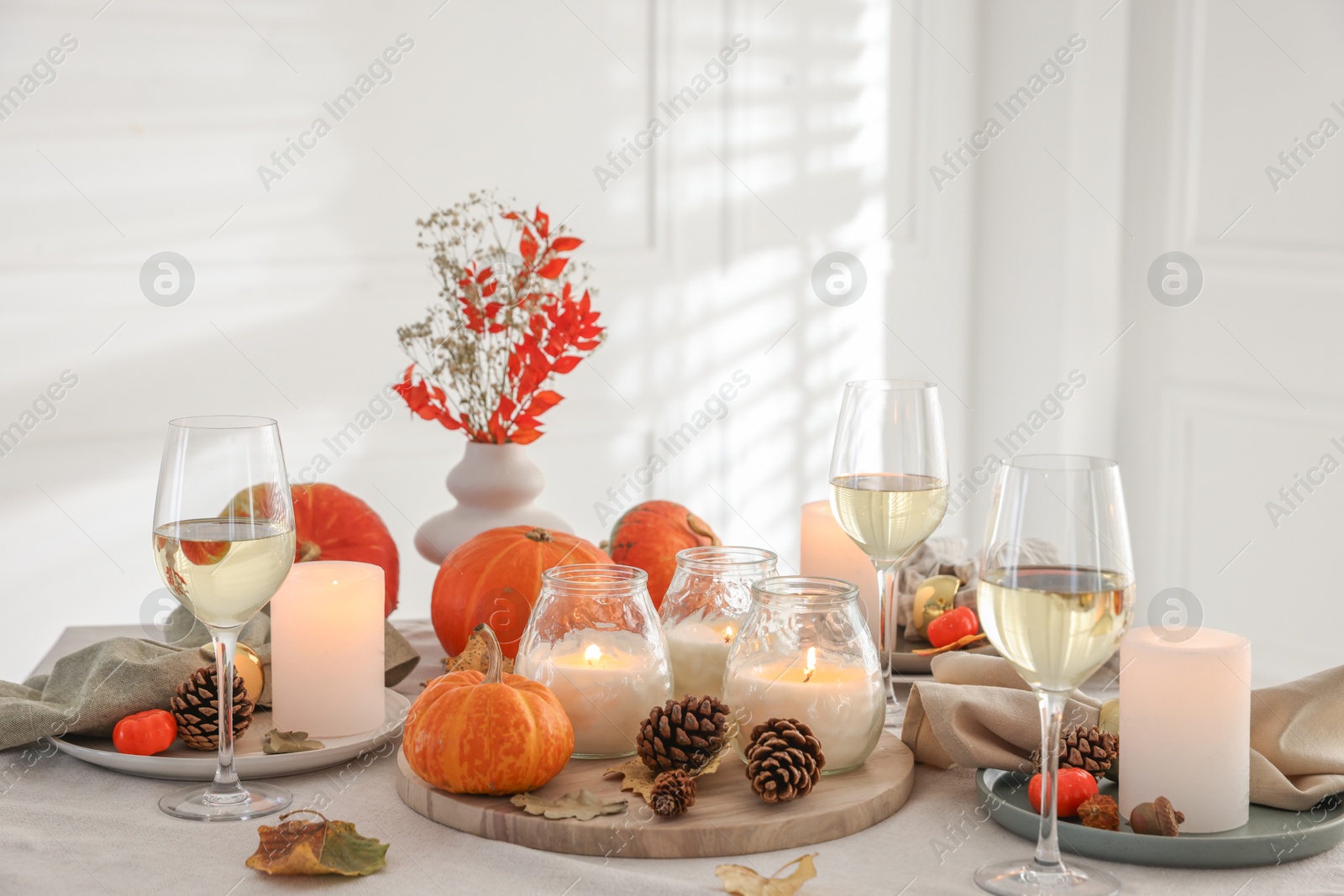 Photo of Autumn place setting with burning candles, glasses of wine and decor on table indoors