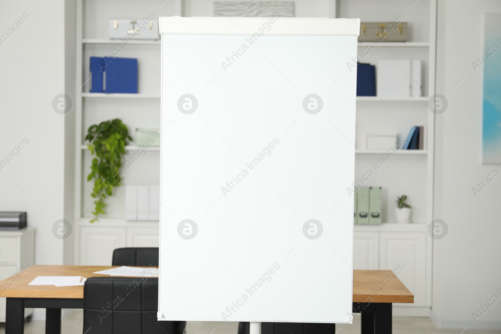 Photo of Flip chart, wooden table and chairs in conference room. Mockup for design