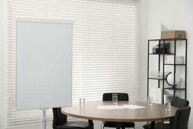 Photo of Flip chart, wooden table and chairs in conference room. Mockup for design