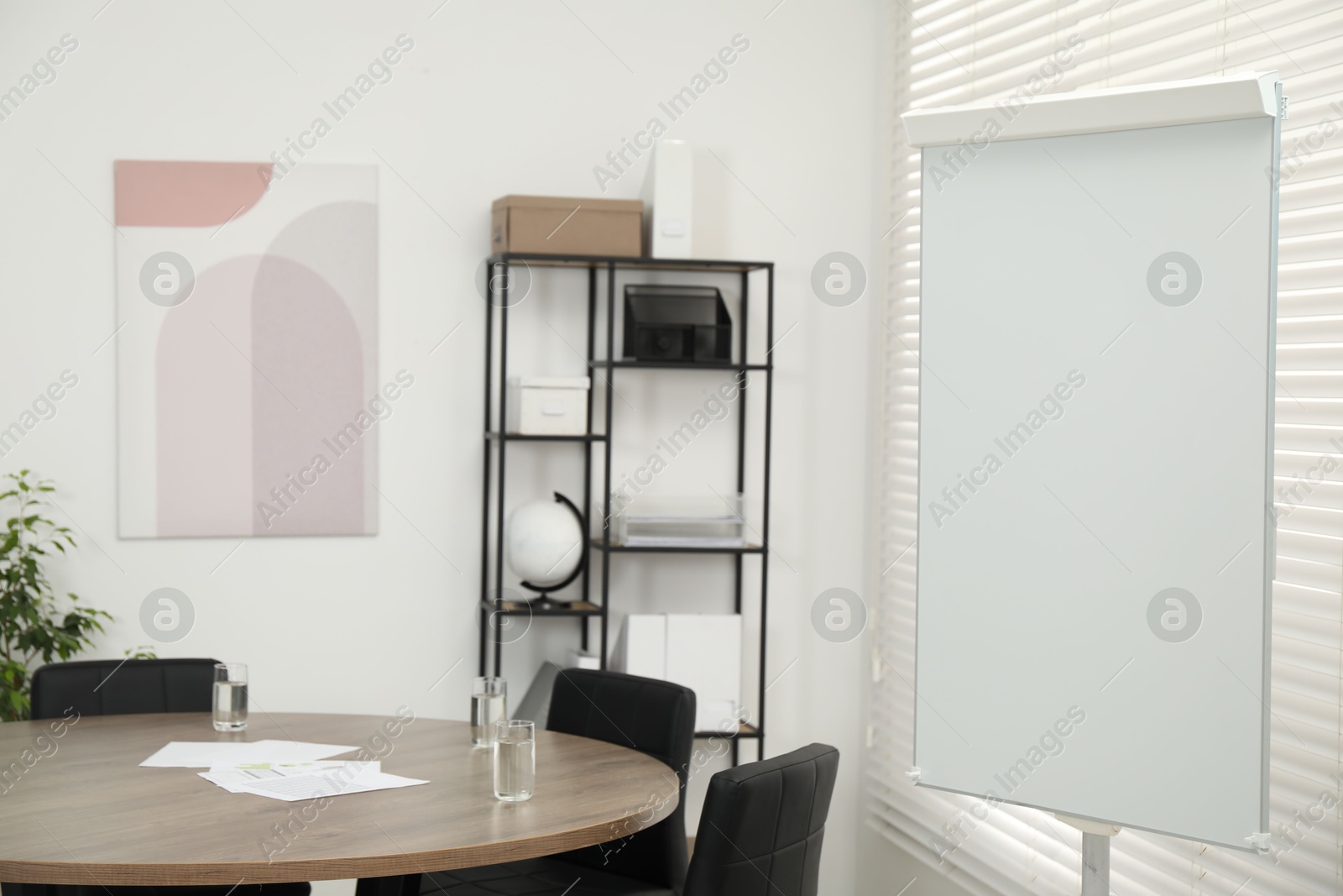 Photo of Flip chart, wooden table and chairs in conference room. Mockup for design