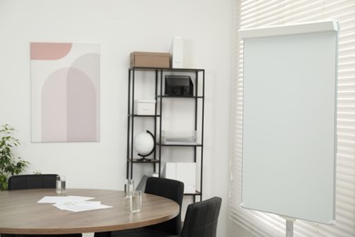 Flip chart, wooden table and chairs in conference room. Mockup for design