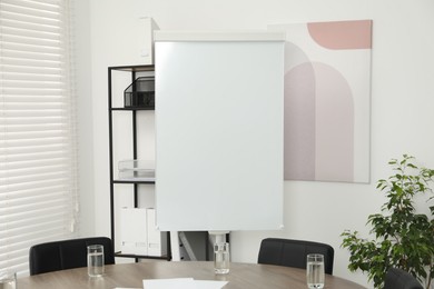 Photo of Flip chart, wooden table and chairs in conference room. Mockup for design