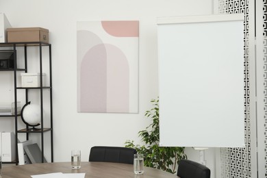 Photo of Flip chart, wooden table and chairs in conference room. Mockup for design