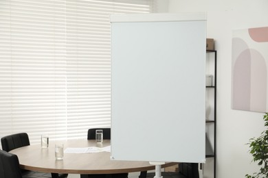 Photo of Flip chart, wooden table and chairs in conference room. Mockup for design