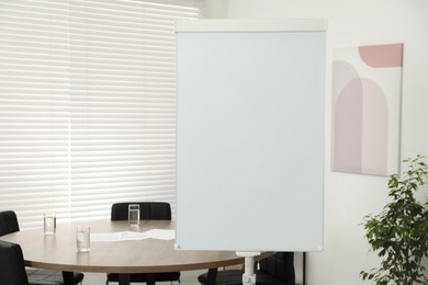 Flip chart, wooden table and chairs in conference room. Mockup for design