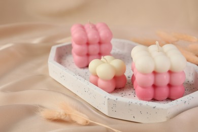 Photo of Beautiful bubble candles and dry spikes on beige fabric, closeup