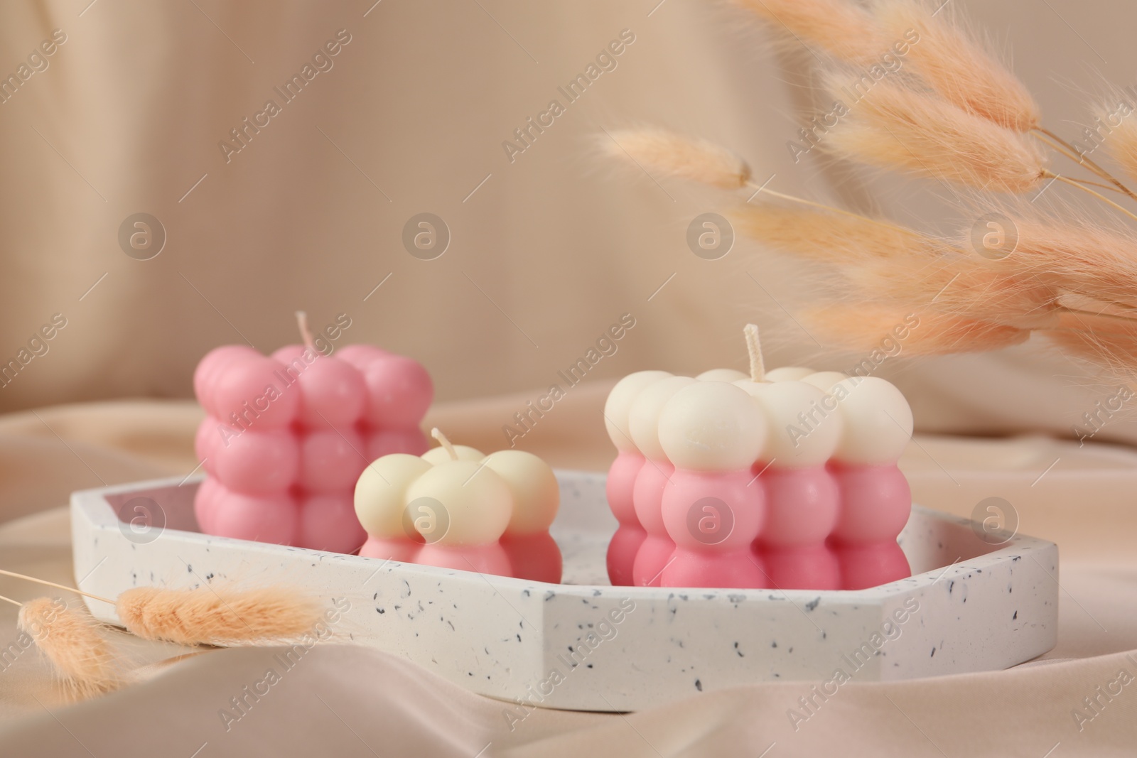 Photo of Beautiful bubble candles and dry spikes on beige fabric