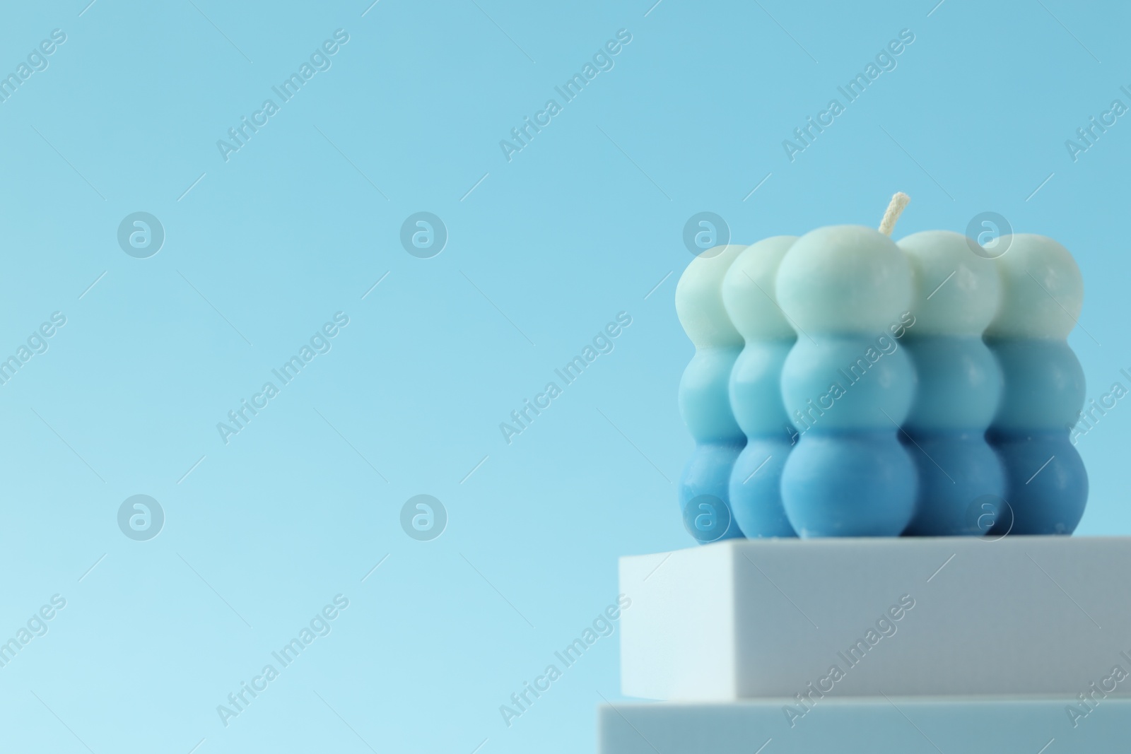 Photo of Beautiful bubble candle and podium on light blue background, closeup. Space for text