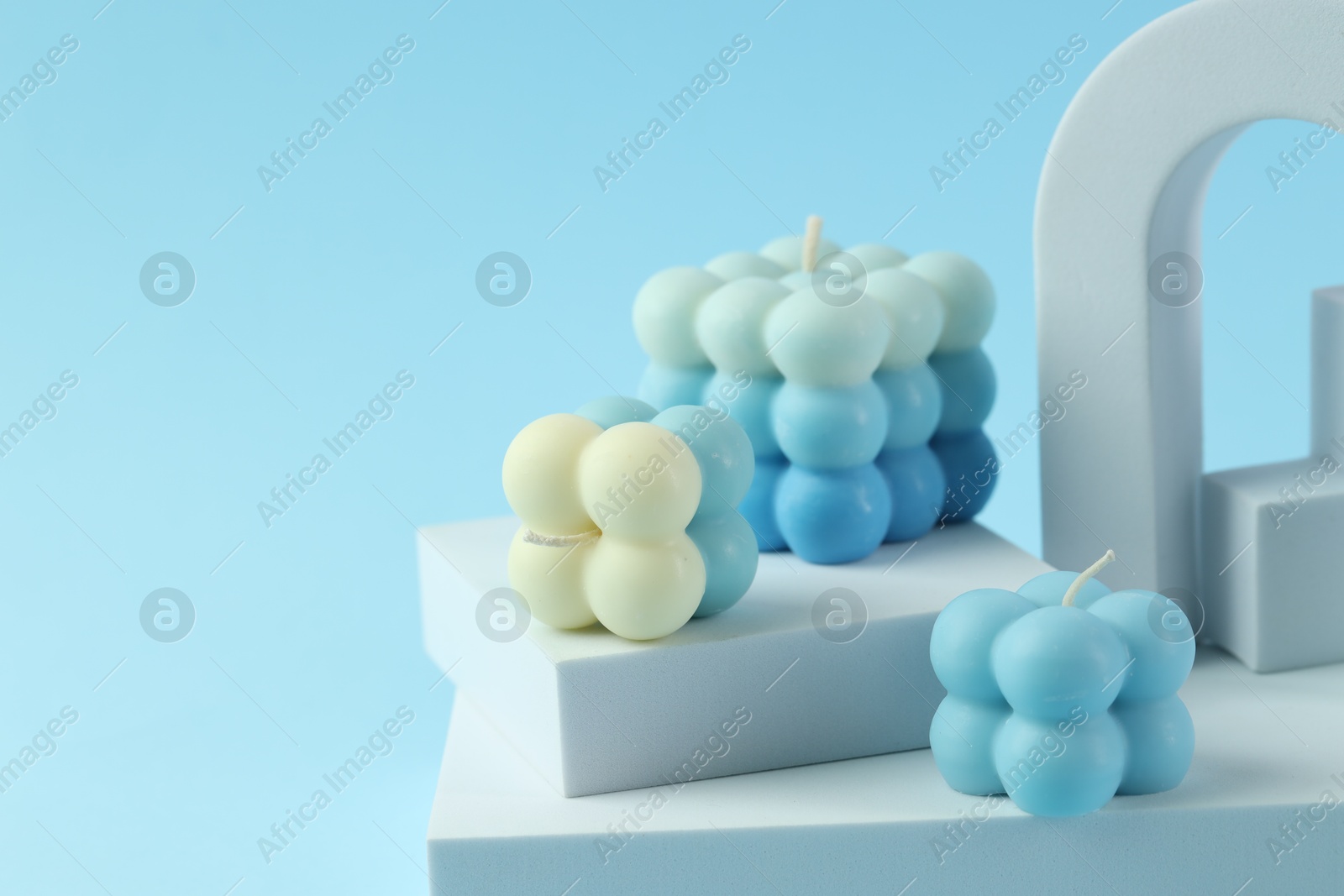 Photo of Beautiful bubble candles and geometric figures on light blue background, closeup