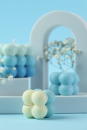 Photo of Beautiful bubble candles, gypsophila flowers and geometric figures on light blue background, closeup