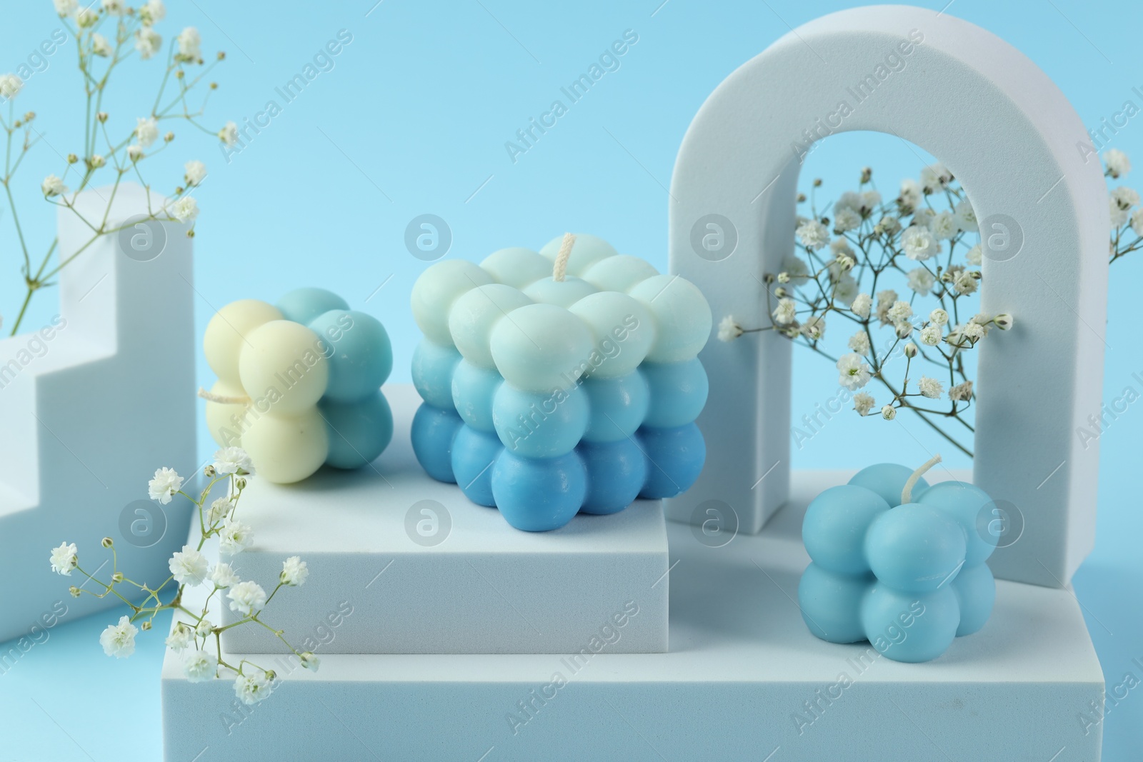 Photo of Beautiful bubble candles, gypsophila flowers and geometric figures on light blue background, closeup