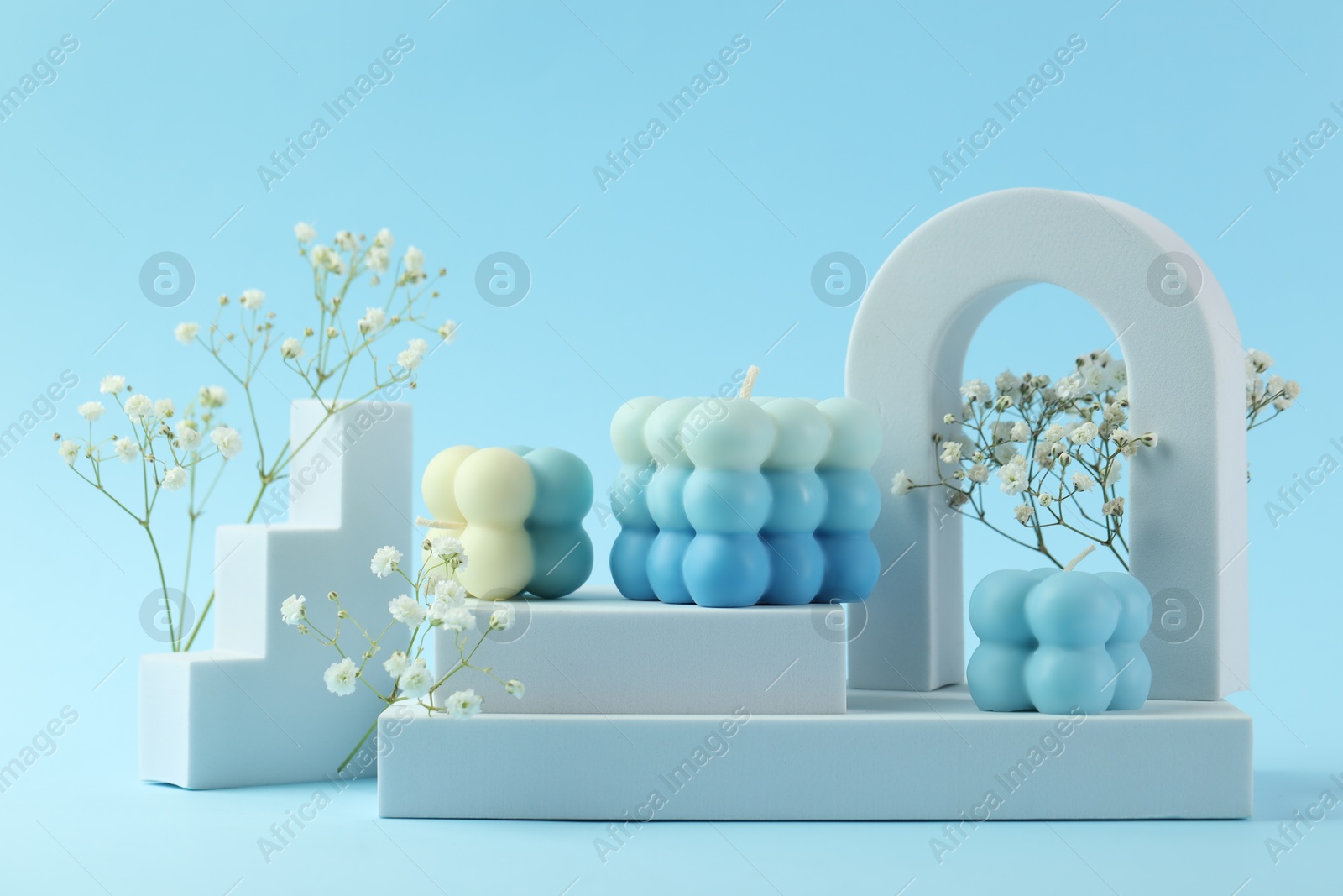 Photo of Beautiful bubble candles, gypsophila flowers and geometric figures on light blue background