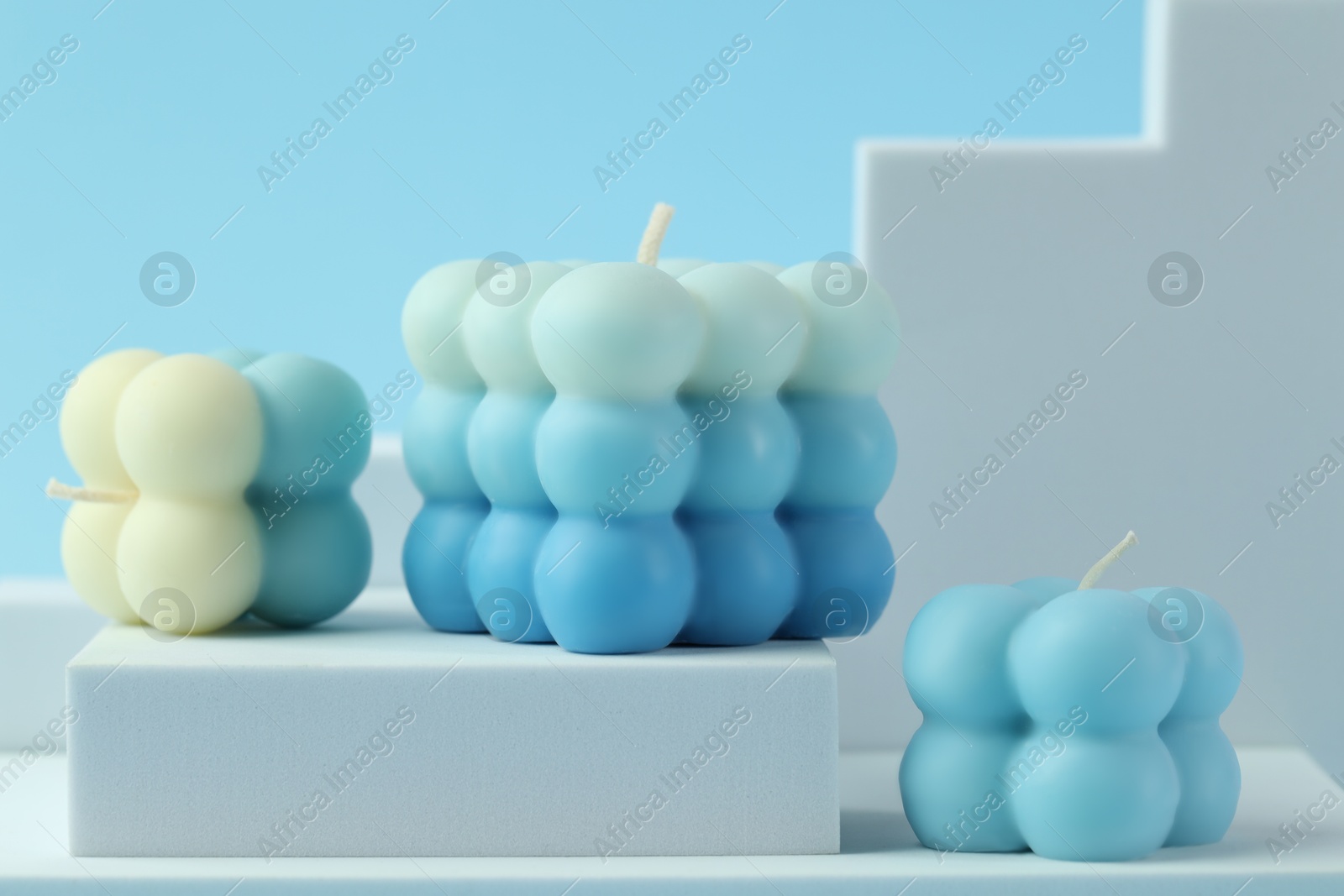 Photo of Beautiful bubble candles and geometric figures on light blue background, closeup