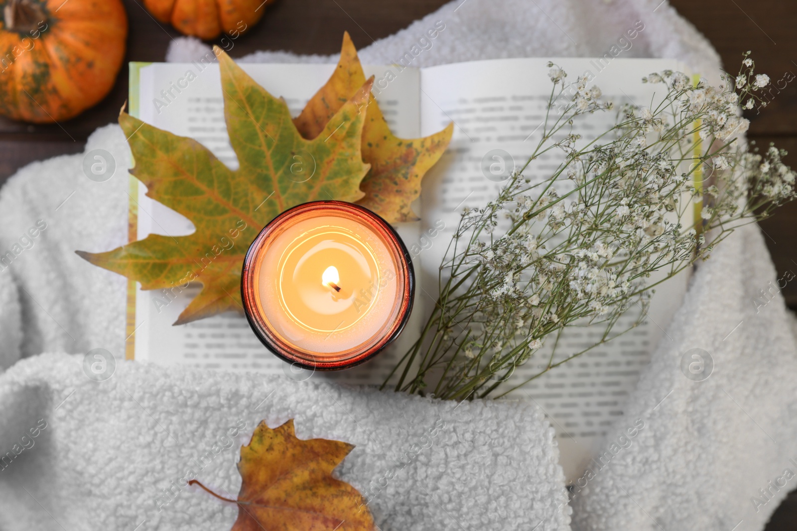 Photo of Burning candle, open book, sweater and autumn decor on table, top view