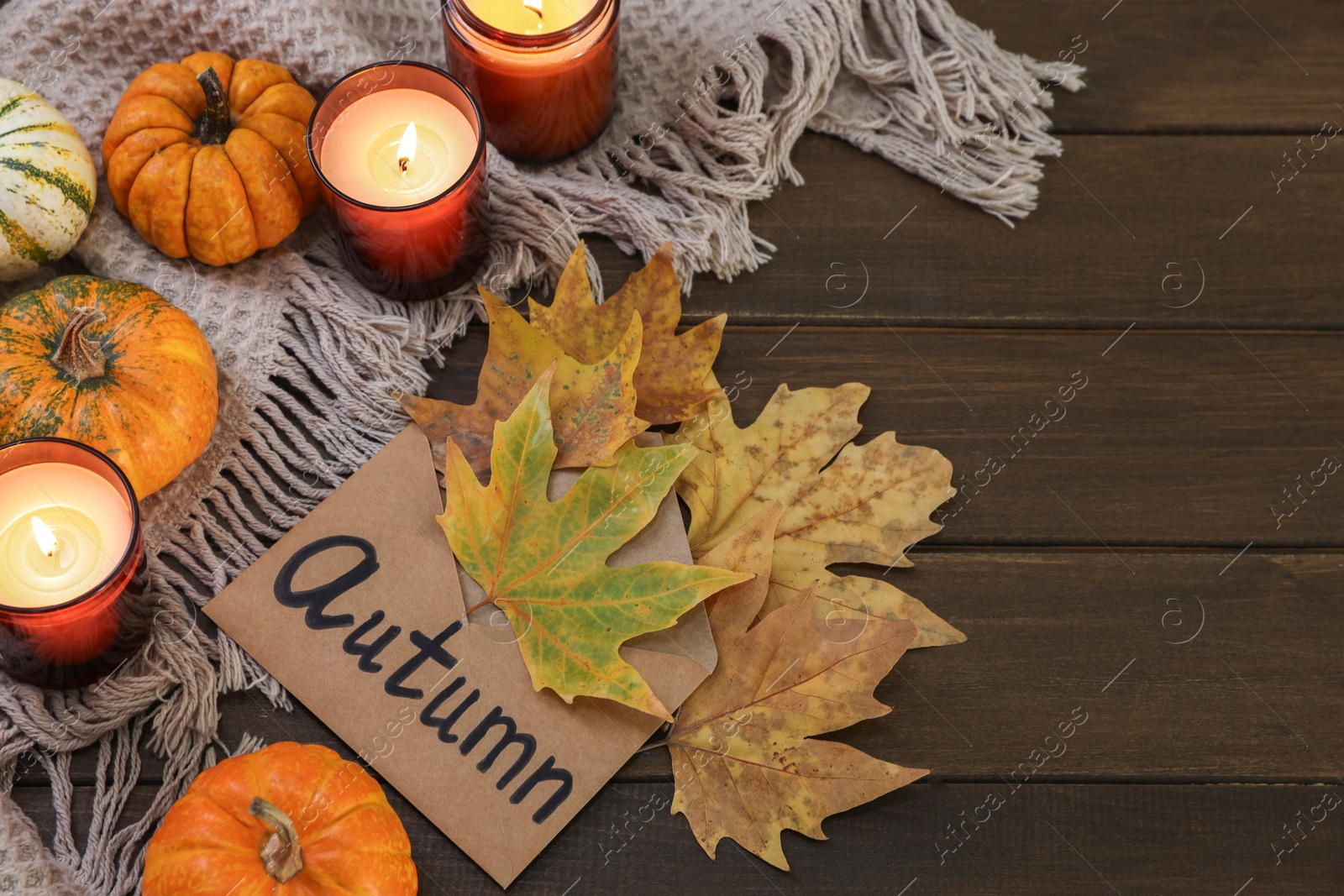 Photo of Envelope with word Autumn, burning candles, dry leaves and pumpkins on wooden table, above view