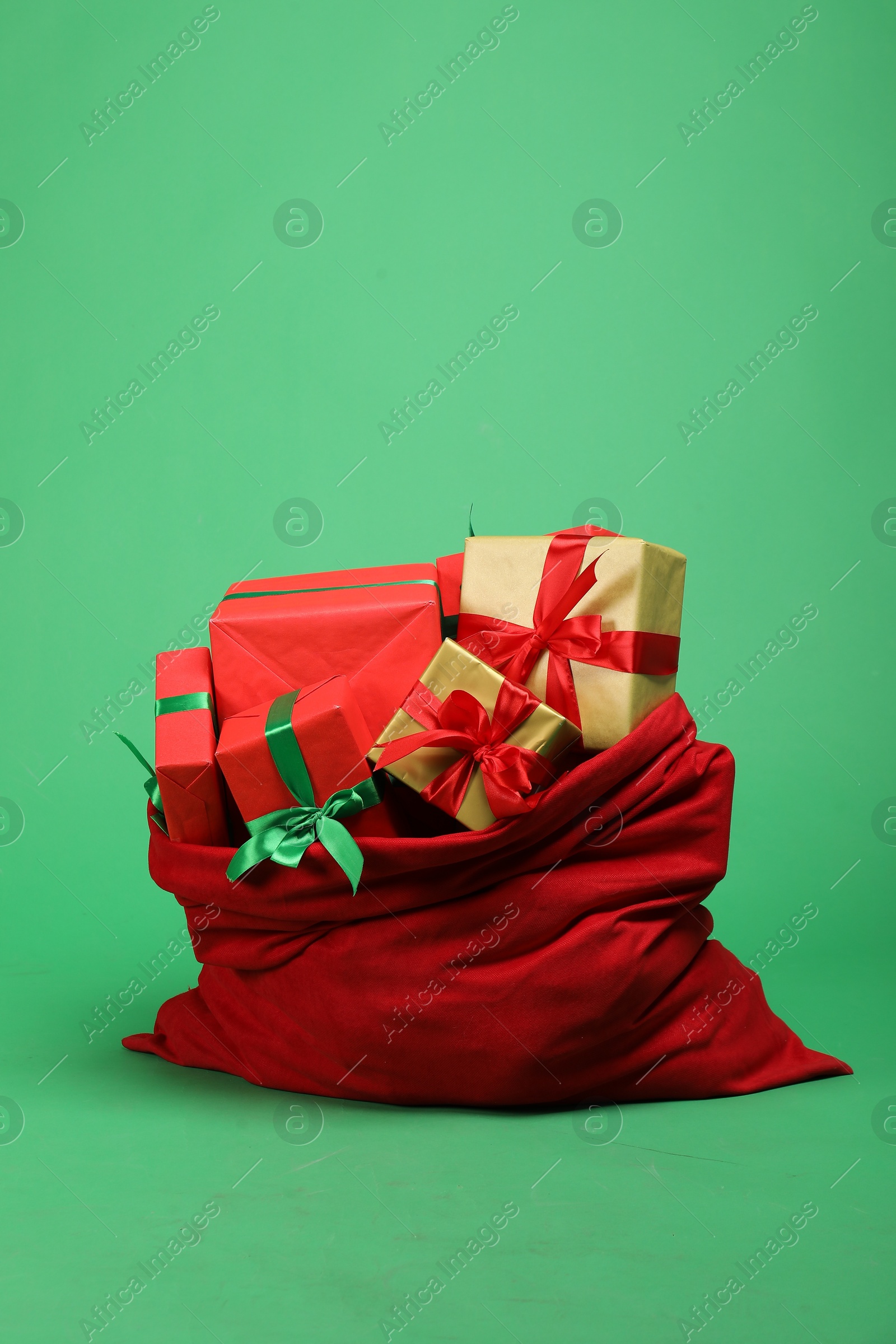 Photo of Red Santa Claus bag with gift boxes on green background