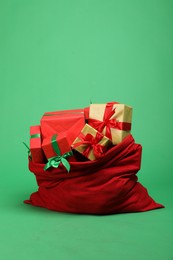 Photo of Red Santa Claus bag with gift boxes on green background