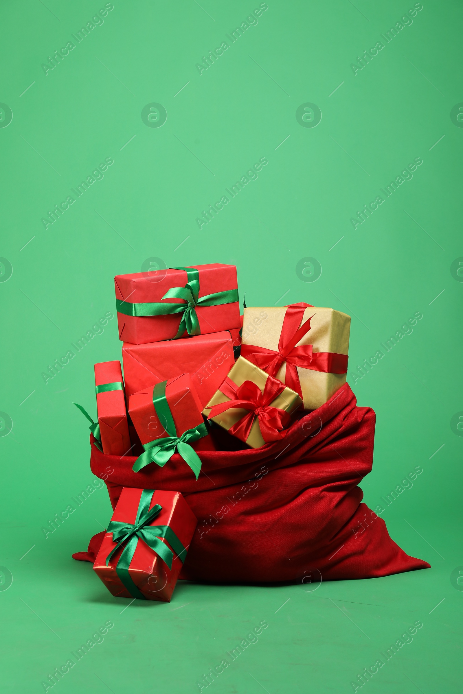 Photo of Red Santa Claus bag with gift boxes on green background