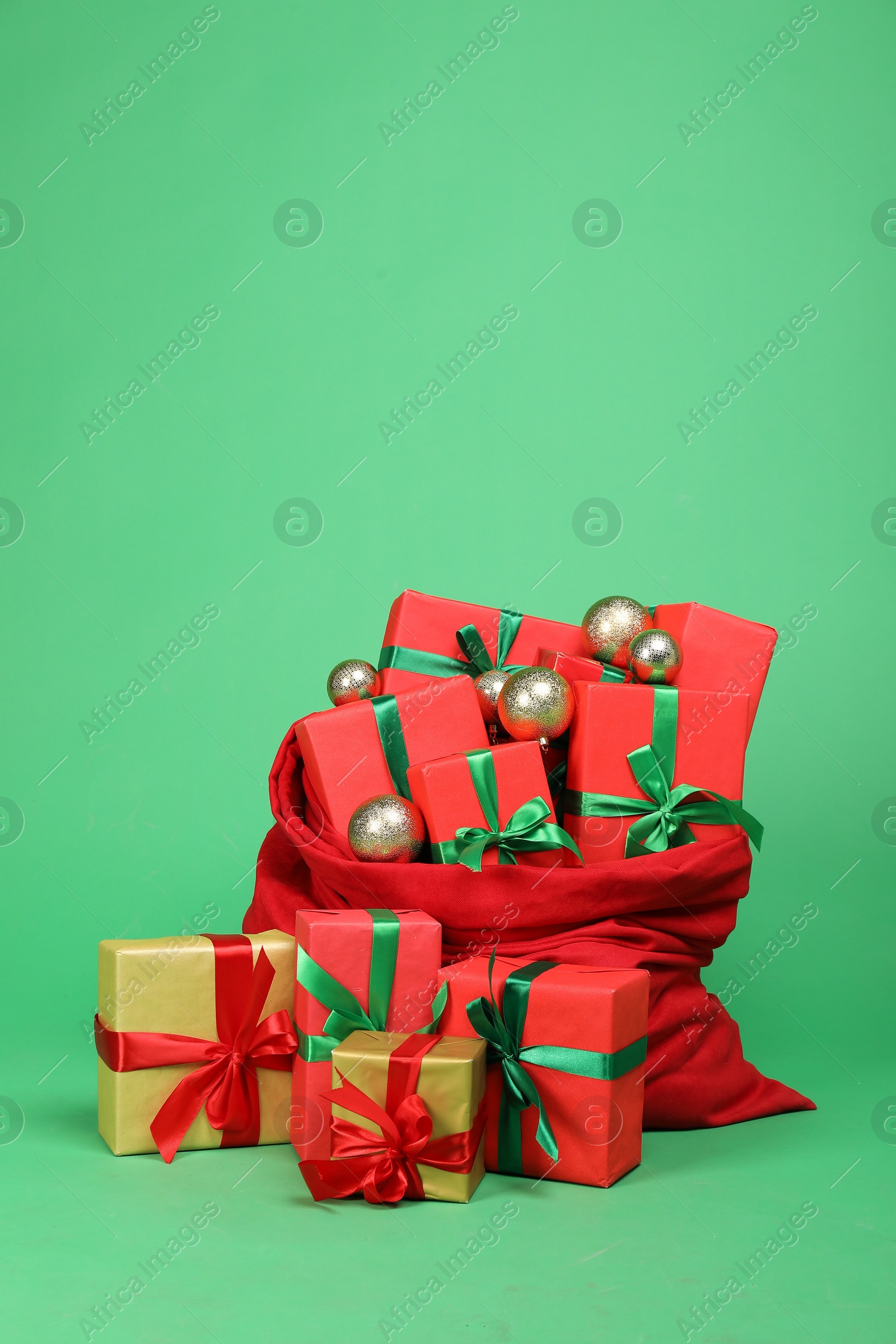 Photo of Red Santa Claus bag with baubles and gift boxes on green background