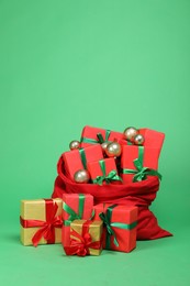 Photo of Red Santa Claus bag with baubles and gift boxes on green background