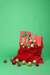 Photo of Red Santa Claus bag with baubles and gift boxes on green background