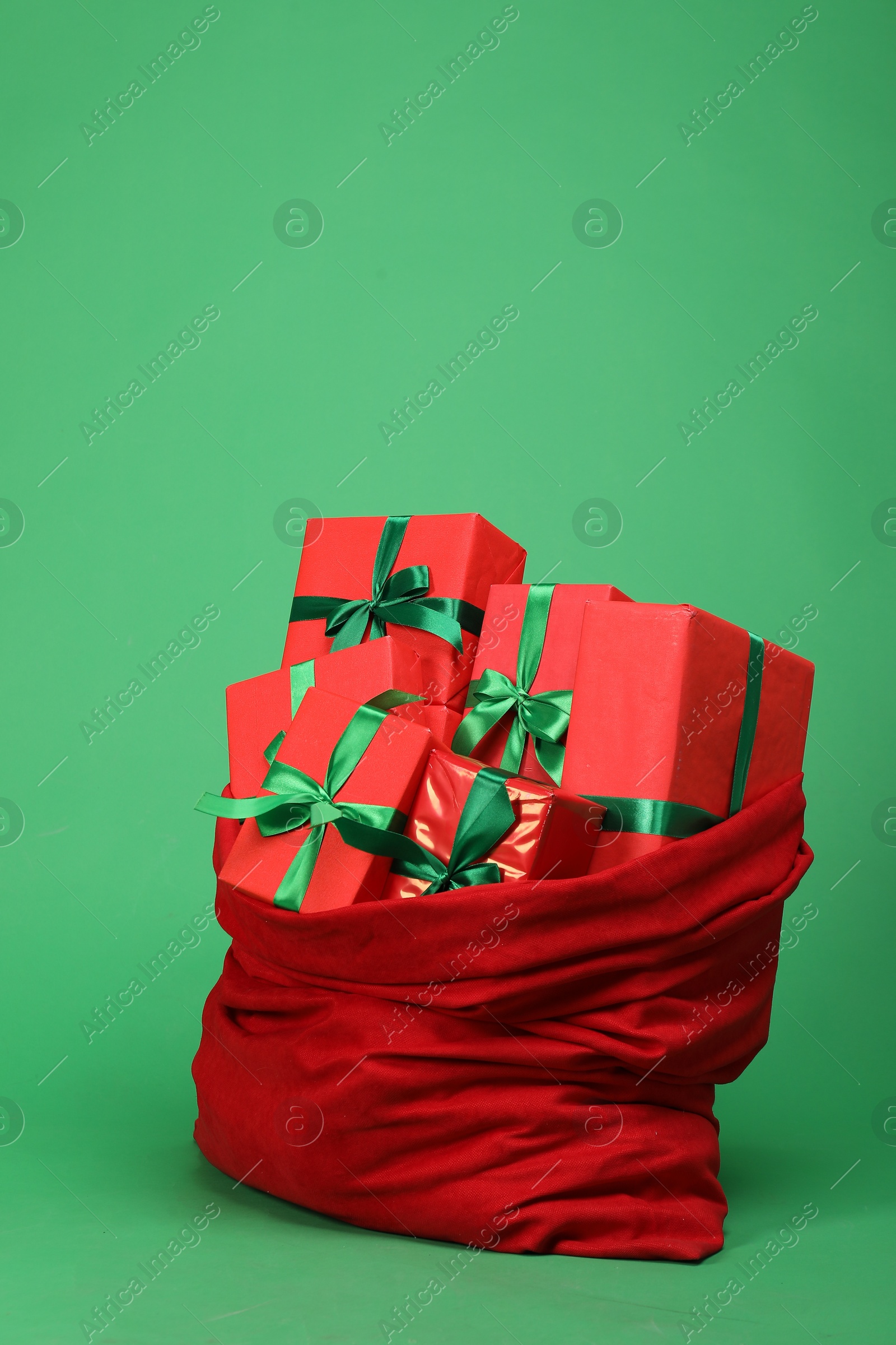 Photo of Red Santa Claus bag with gift boxes on green background