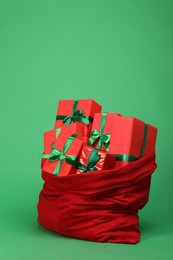 Photo of Red Santa Claus bag with gift boxes on green background