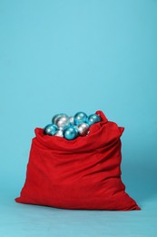 Photo of Santa Claus bag with baubles on light blue background