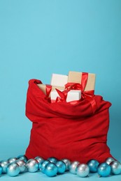 Photo of Santa Claus bag with baubles and gift boxes on light blue background