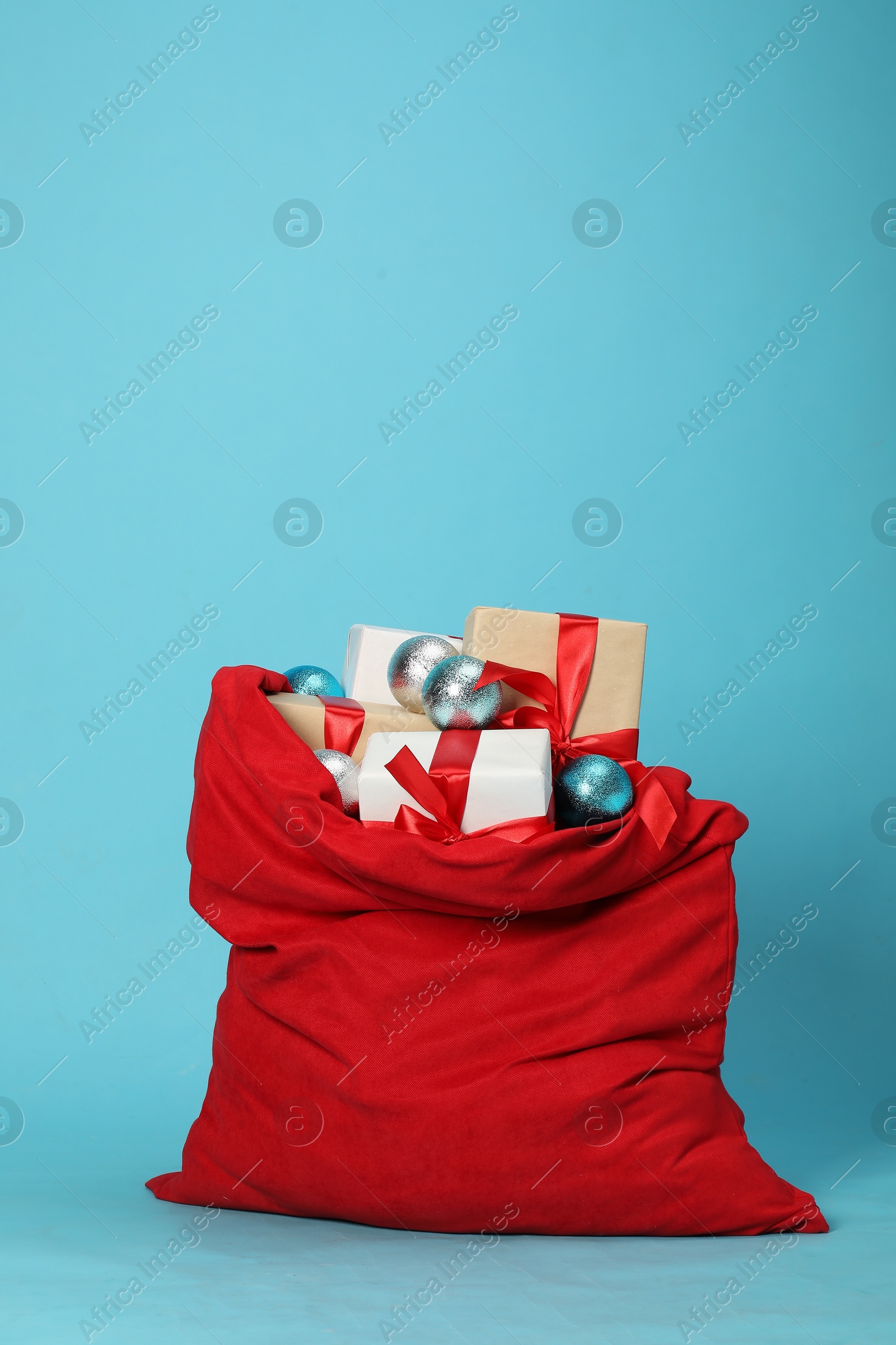 Photo of Santa Claus bag with baubles and gift boxes on light blue background