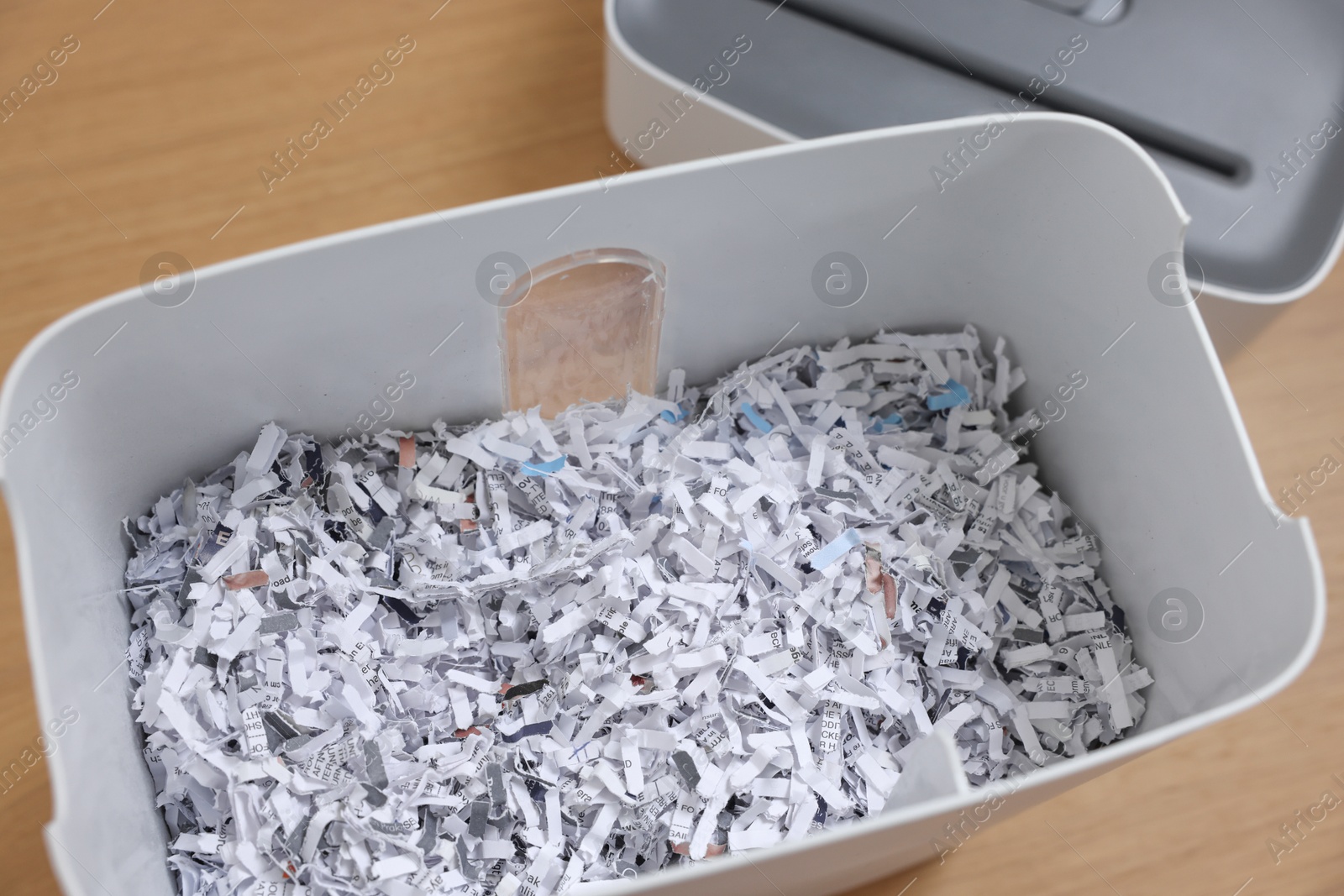 Photo of Shredder and basket with paper strips on wooden table