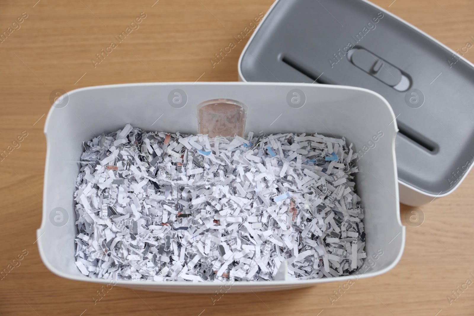 Photo of Shredder and basket with paper strips on wooden table, top view