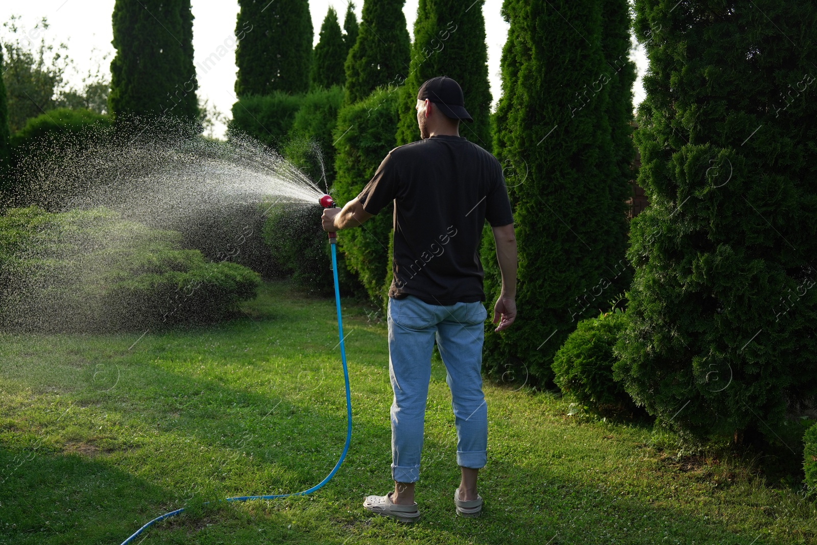 Photo of Man watering lawn with hose in backyard