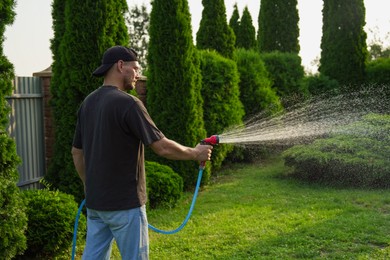 Photo of Man watering lawn with hose in backyard