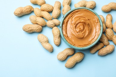 Photo of Tasty peanut butter in bowl and groundnuts on light blue background, flat lay. Space for text